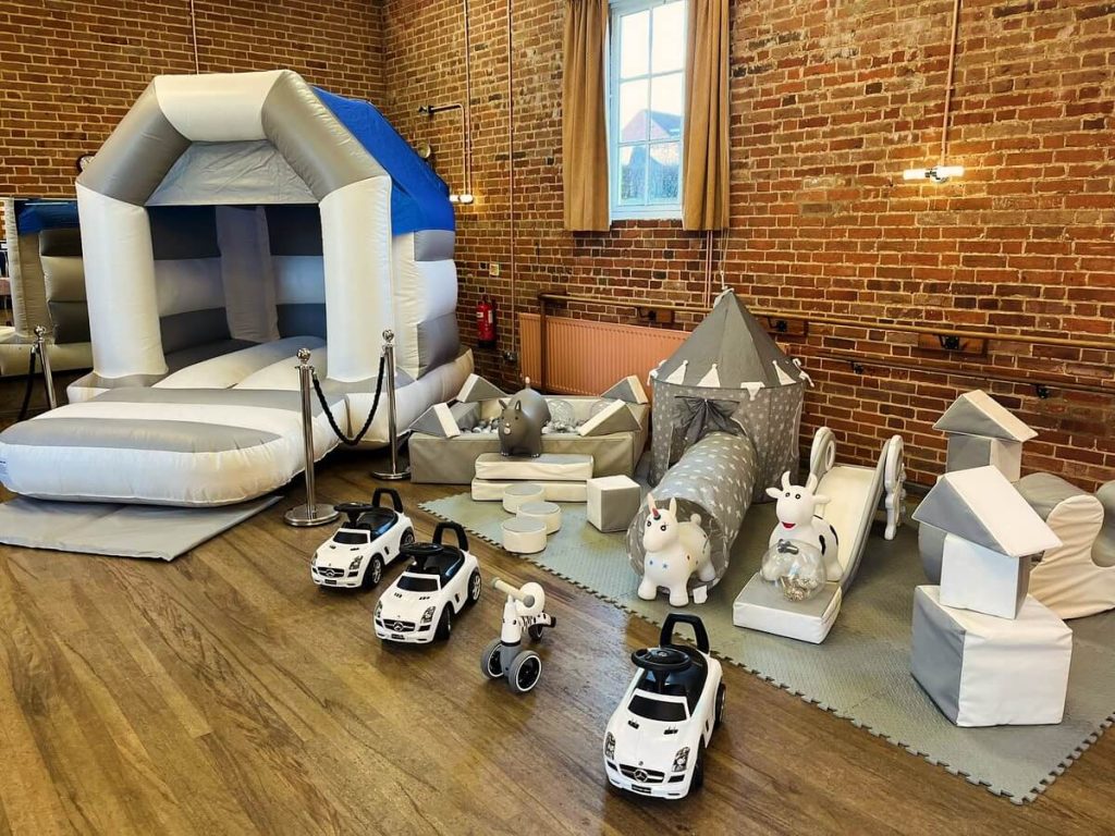 White and grey children's soft play equipment setup and complete with a bouncy castle, ride on cars and a ball pit.